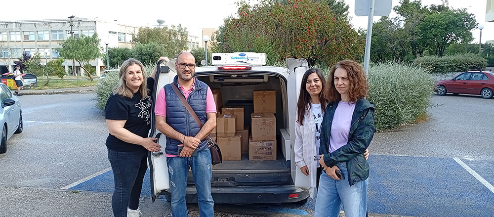 Τέσσερα άτομα μπροστά από ένα μικρό φορτηγό με ανοικτές πόρτες που φαίνονται μέσα του κούτες με τρόφιμα.